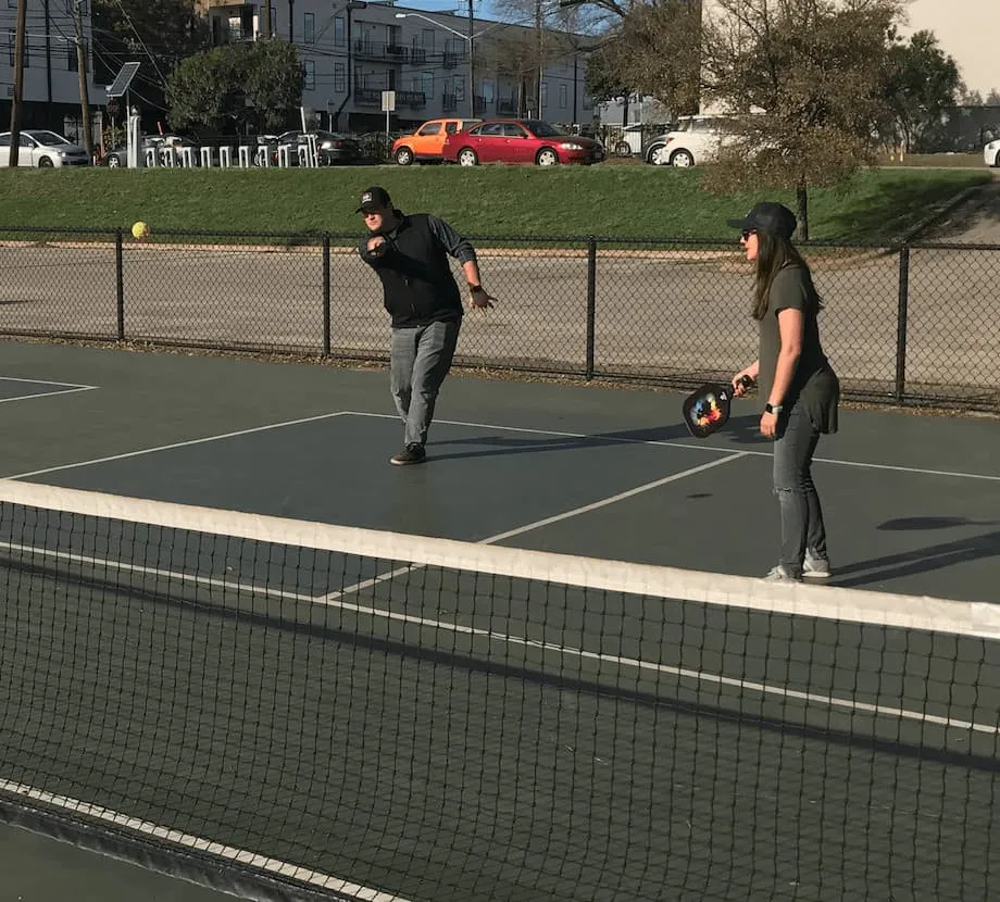 Two coworkers playing pickleball on an outdoor court on a sunny afternoon