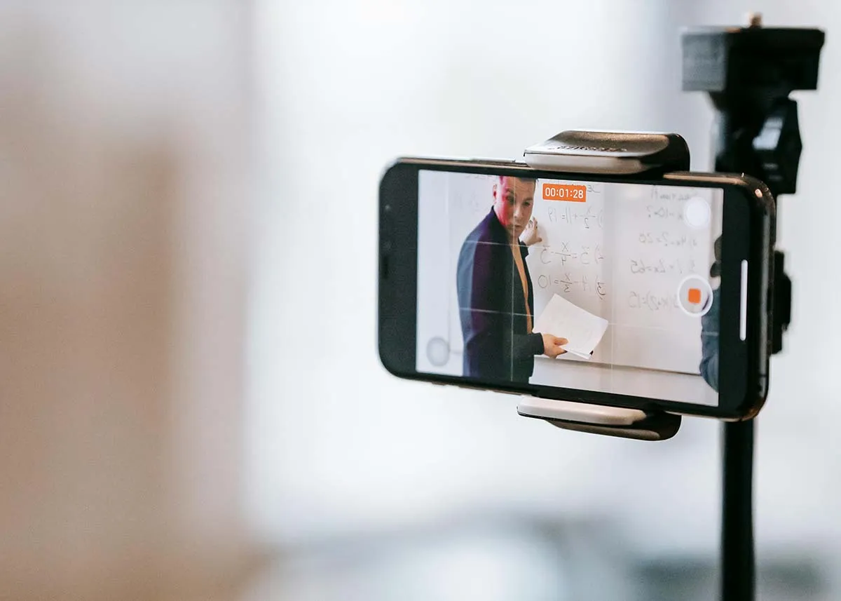 A smartphone mounted on a tripod recording a livestream of a presenter standing at a whiteboard
