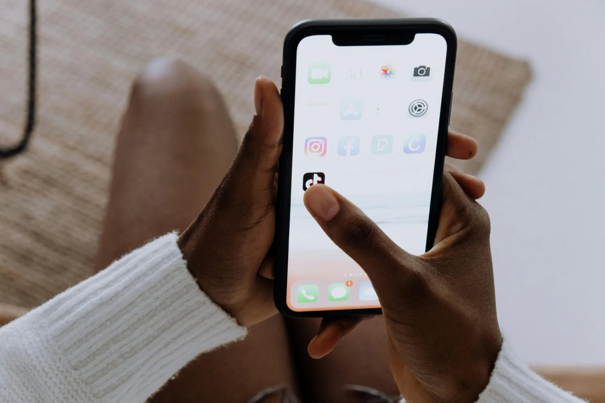 Hands holding an iPhone with the home screen showing social and shopping apps including TikTok, Instagram, and Facebook